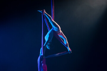 Female circus gymnast hanging upside down on aerial silk and demonstrates stretching. Young woman...
