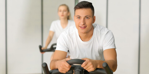 Young man training on exercise bike in gym