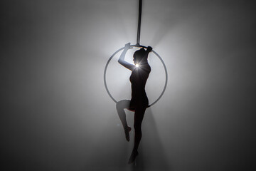 Silhouette of flexible aerial gymnast on an aerial ring performs acrobatic tricks in the air. Young...