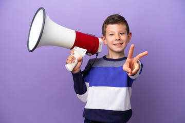 Little boy isolated on purple background holding a megaphone and smiling and showing victory sign
