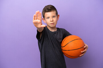 Little boy playing basketball isolated on purple background making stop gesture