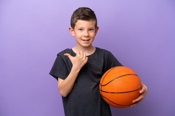 Little boy playing basketball isolated on purple background pointing to the side to present a...