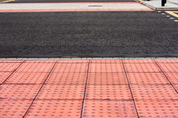 Tactile tiles for the blind. Panels for the blind laid on asphalt. Guide tape for the disabled. Red new tactile tiles for the visually impaired. Equipped modern pedestrian crossing with new asphalt.