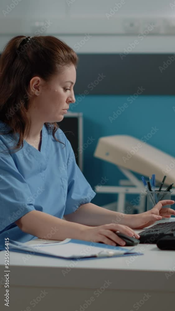 Poster vertical video: medical assistant working on computer with patient information at desk. woman nurse 
