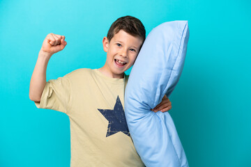 Little boy in pajamas isolated on blue background celebrating a victory