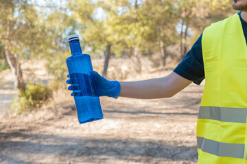 Detalle de brazo, de hombre voluntario cogiendo una botella, en la montaña. Fotografía horizontal...