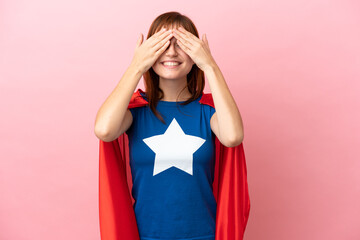 Super Hero redhead girl isolated on pink background covering eyes by hands