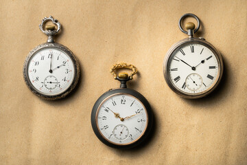 Set of three antique silver pocket watches with golden clockwork on beige background. Retro...