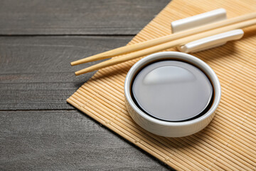 Bowl of soy sauce, chopsticks and bamboo mat on dark wooden background, closeup