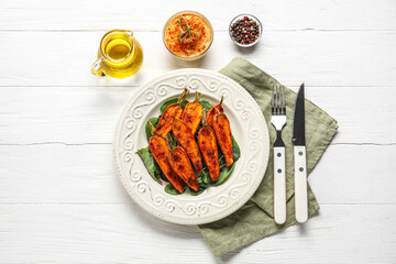 Composition with plate of tasty baked carrots, spices and cutlery on light wooden background