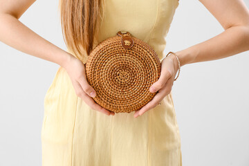 Woman holding stylish rattan handbag on light background, closeup