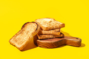 Wooden board with toasts and piece of butter on yellow background
