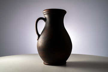 Brown earthenware jug with a handle in a dark studio. An old jar from clay standing on a white...