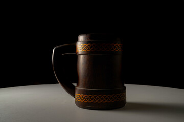 Wooden oak mug with a handle on white table isolated on black studio background. Brown mug with...