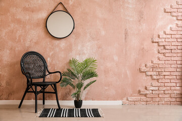 Stylish chair, houseplant and mirror hanging on pink wall