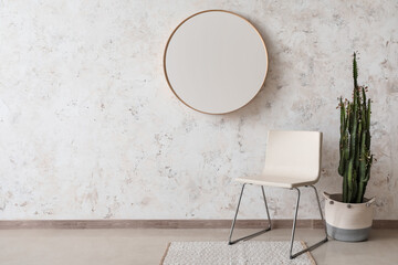 Stylish chair, cactus and mirror hanging on light wall