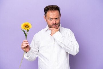 Middle age caucasian man holding sun flower isolated on purple background thinking