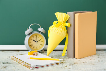 School cone with books and alarm clock on table near chalkboard