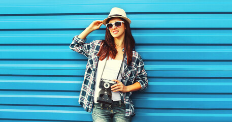 Portrait of young woman photographer with film camera wearing summer straw hat on blue background
