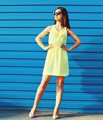 Portrait of beautiful brunette young woman wearing yellow dress on blue background