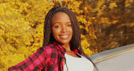 Portrait of young smiling african woman with dreadlocks in autumn park