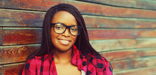 Close up portrait of modern young smiling african woman wearing eyeglasses in the city on wooden background