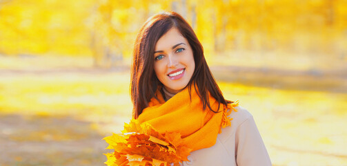 Portrait of beautiful brunette smiling woman wearing scarf with yellow maple leaves in autumn park