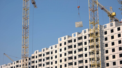 Fototapeta na wymiar Yellow crane lifts up concrete floor on the building. Blue sky background.