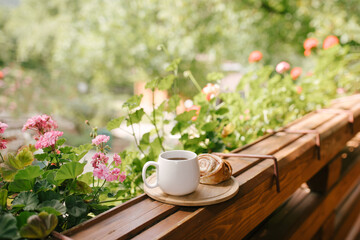 Mug with tea and cinnabon on tray on cozy balcony of wooden cottage.