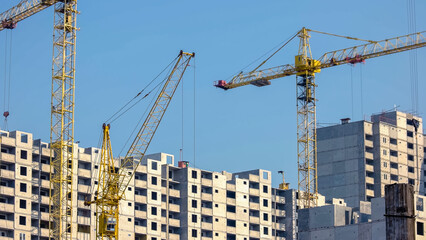 Fototapeta na wymiar Yellow construction cranes and buildings over blue sky background. High-rise skyscrappers under construction.