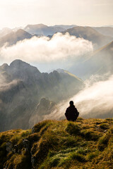 Concept photo for wellbeing, zen yoga moment on top of the mountains in the middle of nature. A woman stands on a mountain peak in a beautiful sunrise landscape.