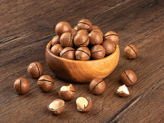 Macadamia nuts in a wooden bowl and on a wooden background.