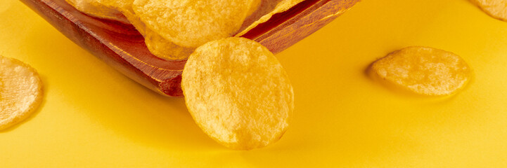 Potato chips or crisps, a salty snack on a yellow background, a panoramic banner