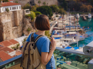 Obraz premium travel to Turkey, old town Antalya Kaleci. Happy asian female tourist traveller with backpack walks in old city. Woman on lookout over the old town and the port from viewpoint