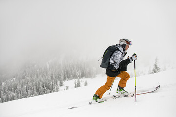 Side view of male skier with trekking poles climbing up snowy mountain slope.