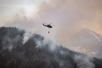 Firefighting helicopter with a bucket suspended on a cable, collecting water from a mountain lake...