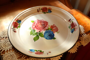 A vintage metal dinner plate with flower motif, on a wooden table.