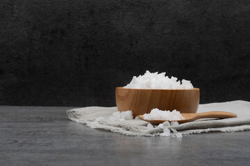 Sea salt in bowl with spoon and cloth on stone texture background