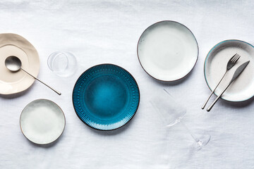 Modern tableware set with cutlery, glasses, and a vibrant blue plate, overhead flat lay shot....