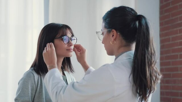 Video of  female doctor choosing while proving eyeglasses to mature beautiful patient in medical consultation.