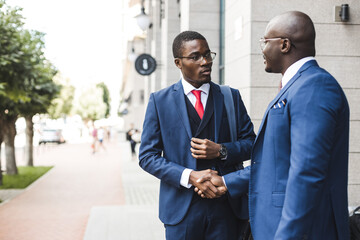 Portrait of two black African American businessman in suits shake hands outdoors. The joy of...
