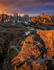 Gardena Pass, Italy - Aerial panoramic view of the curvy roads of the famous Gardena Pass (Passo Gardena) with the peaks of Pizes de Cir, the Italian Dolomites and a warm sunset at autumn season