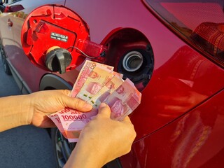 Money for gasoline and fuel.  Gasoline is expensive.  Driver holding big money to pay fuel bill against gas tank background.  the concept of increasing the price of gasoline and fuel