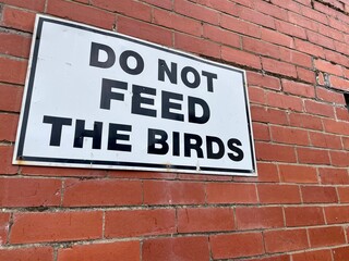 Do not feed birds sign on brick wall - Powered by Adobe