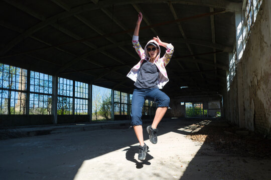 Young female hip hop dancer dancing and jumping in abandoned building on a sunny summer day