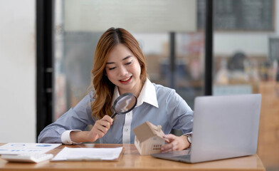 Close up of businesswomen holding magnifying glass finding a wooden shape of a house, realtor, agent, insurance, developer, planning and investment real estate business concept,