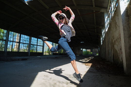 Young female hip hop dancer dancing and jumping in abandoned building on a sunny summer day
