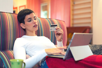 Young woman drinking coffee and shopping online  while lying on the couch at home