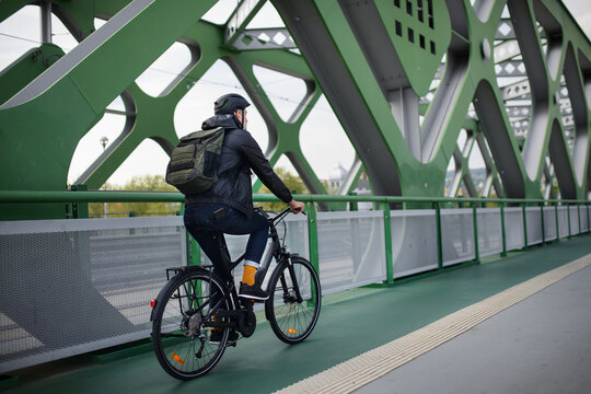 Rear view of businessman commuter on the way to work, riding bike over bridge, sustainable lifestyle concept.