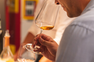 Close up of a man holding a glass of orange wine and smelling it during wine tasting.

